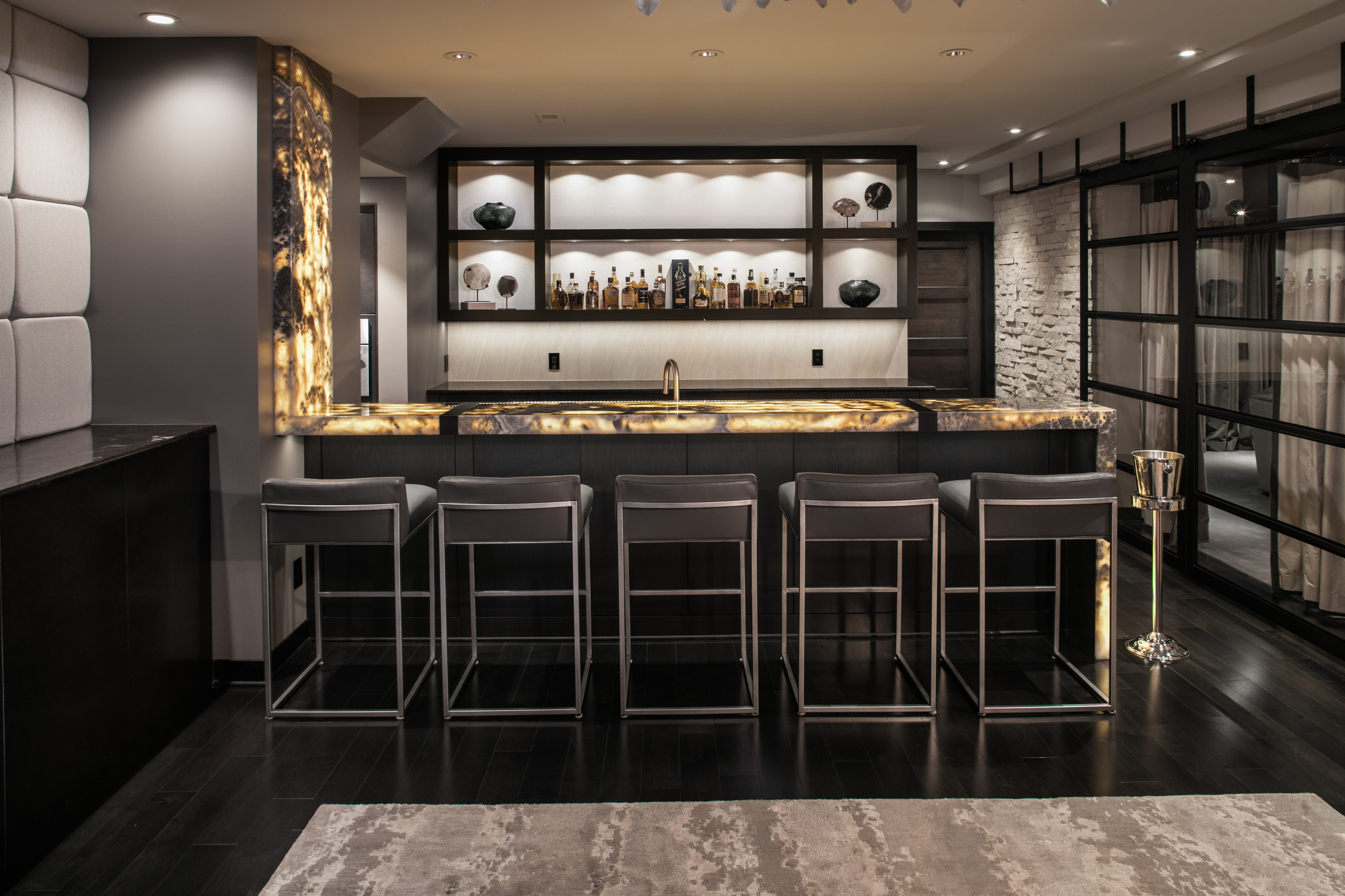luxurious modern home bar with illuminated onyx countertop, sleek shelving, and contemporary bar stools