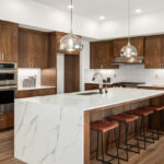 Modern kitchen with dark wood cabinets, waterfall marble island, and stainless steel appliances.