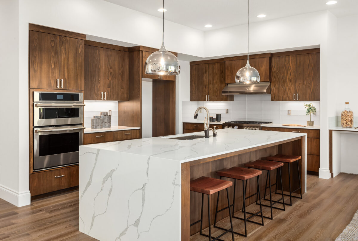 Modern kitchen with dark wood cabinets, waterfall marble island, and stainless steel appliances.