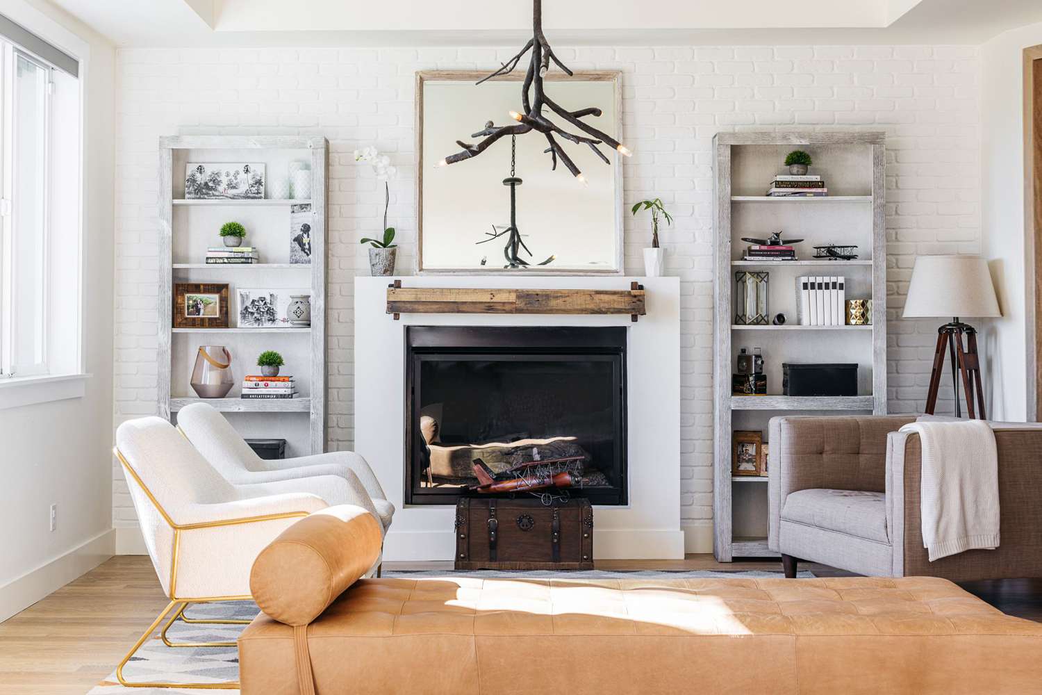 Modern living room with white brick walls, rustic wood mantel fireplace, minimalist shelves, and stylish seating.