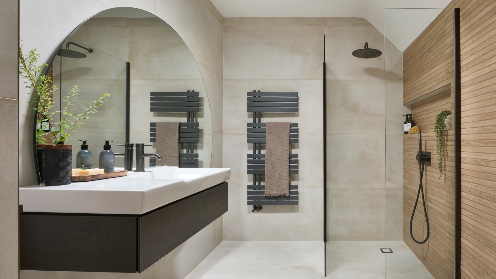 Modern bathroom with large round mirror, wall-mounted sink, and walk-in shower with wood accent wall.