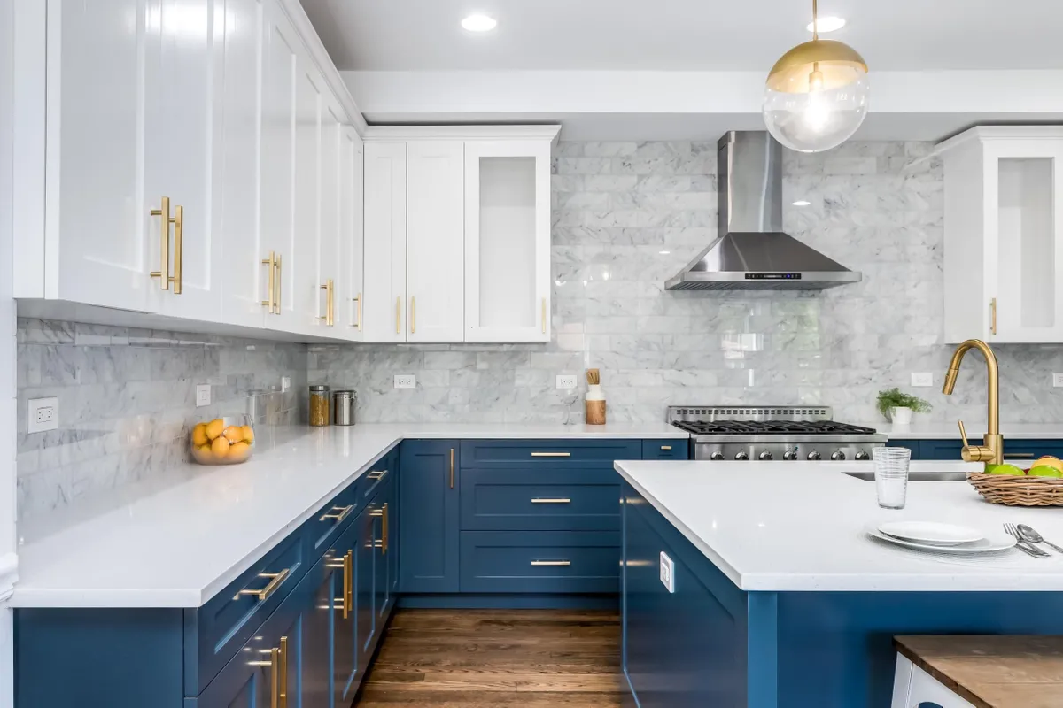 Modern kitchen with two-tone cabinets in navy blue and white, gold hardware, and marble backsplash.