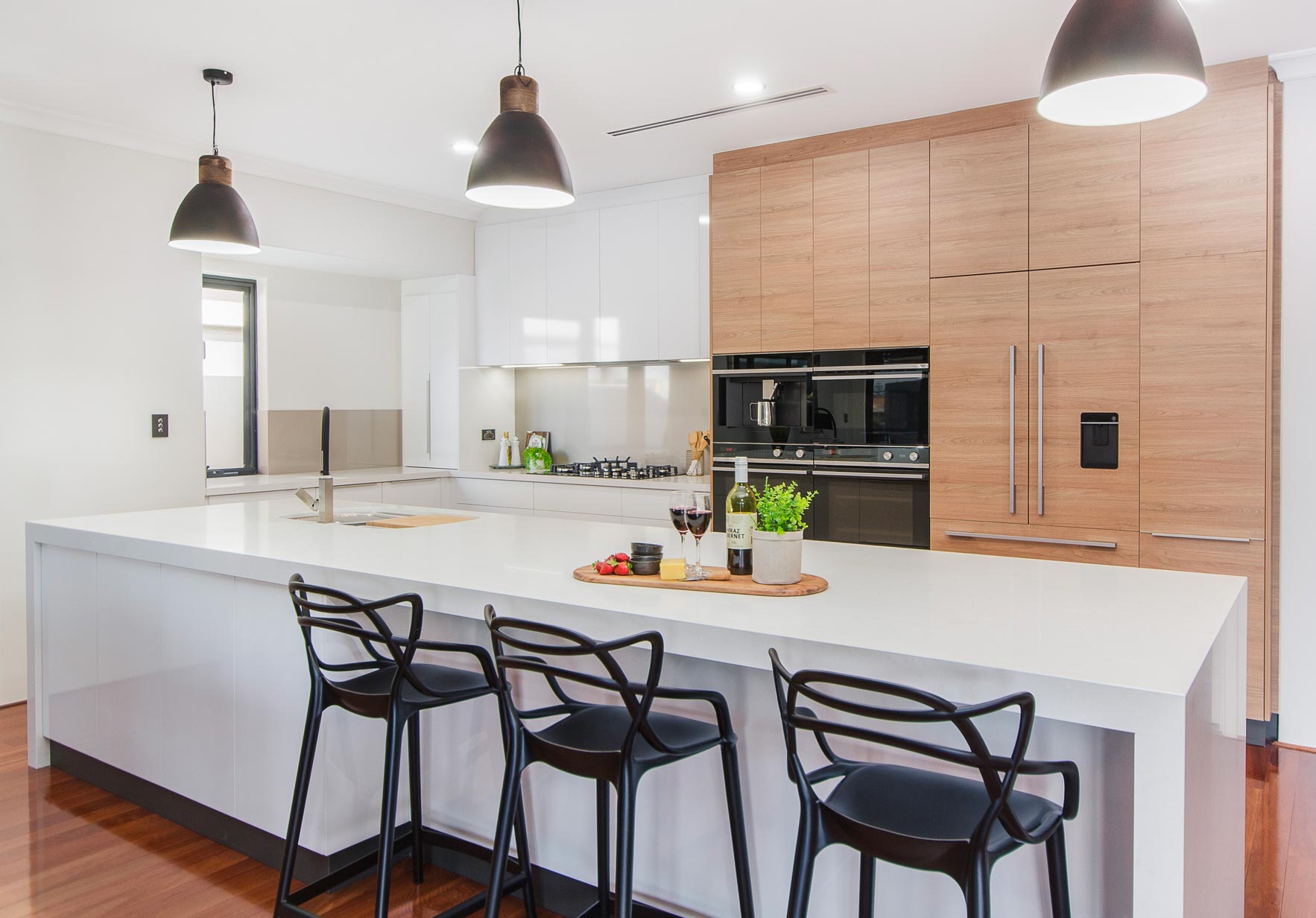 Modern kitchen with white countertops, light wood cabinets, and black barstools.