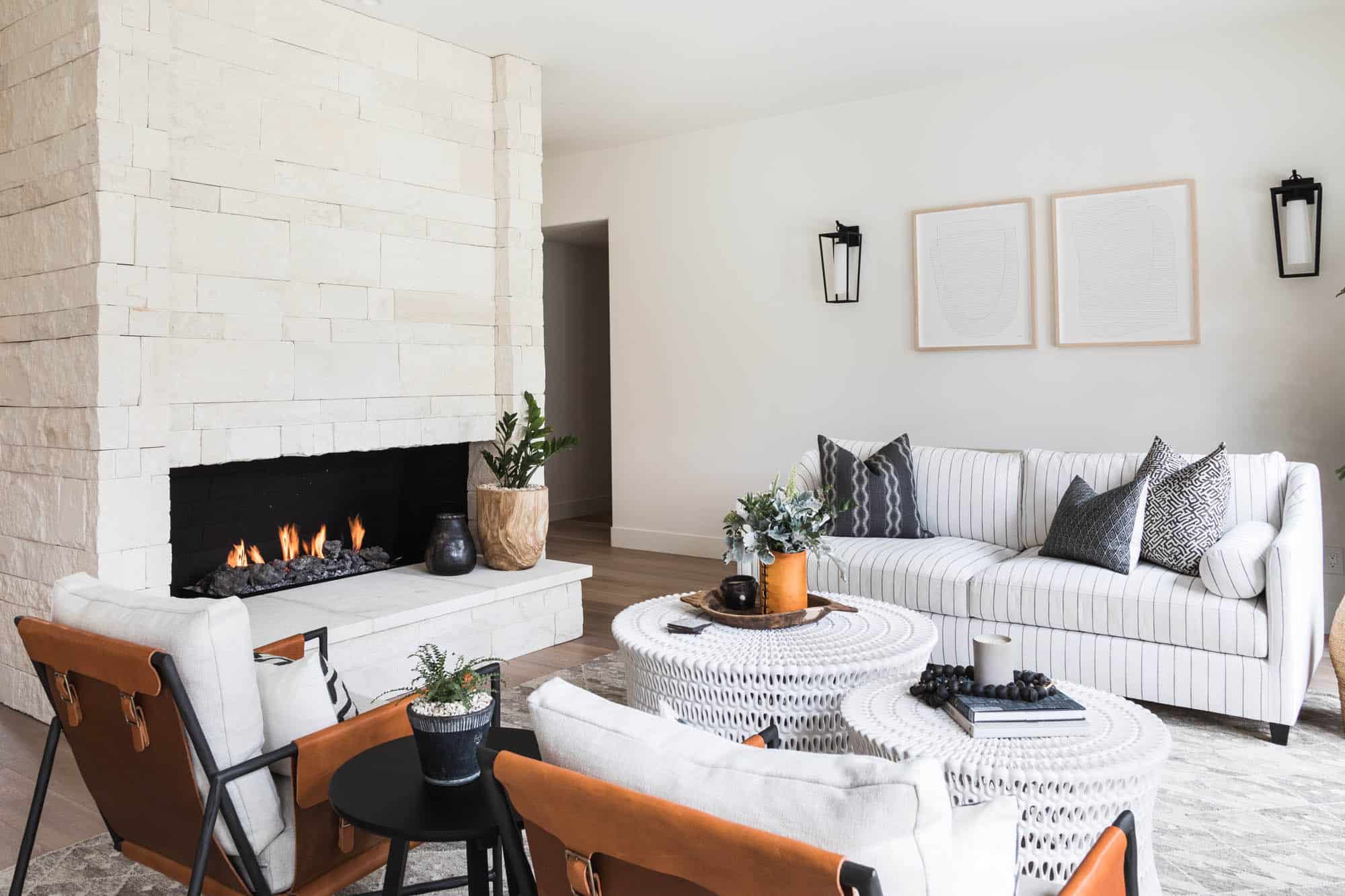 Modern living room with a white stone fireplace, striped sofa, woven coffee tables, and accent chairs with leather details.
