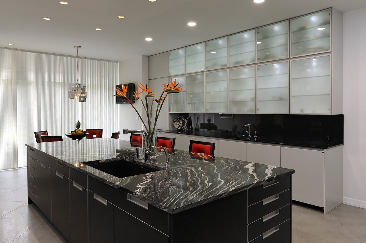 Modern kitchen with black and white cabinetry, a bold black granite island with white veining, and frosted glass upper cabinets.