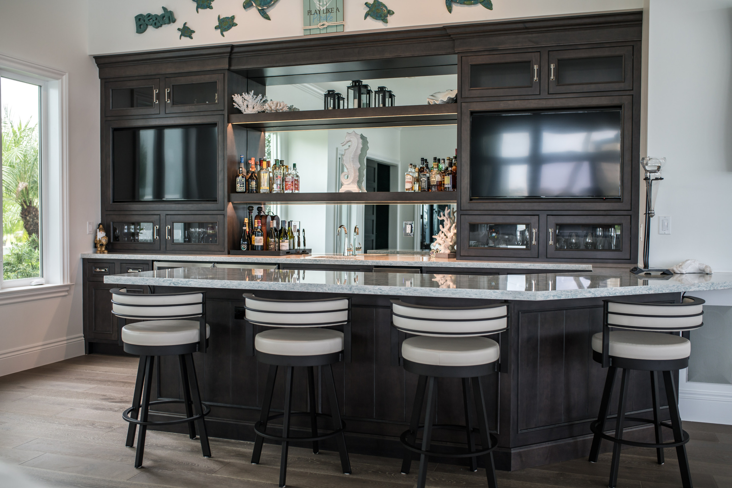 coastal-inspired home bar with dark cabinetry, granite countertop, and light upholstered bar stools