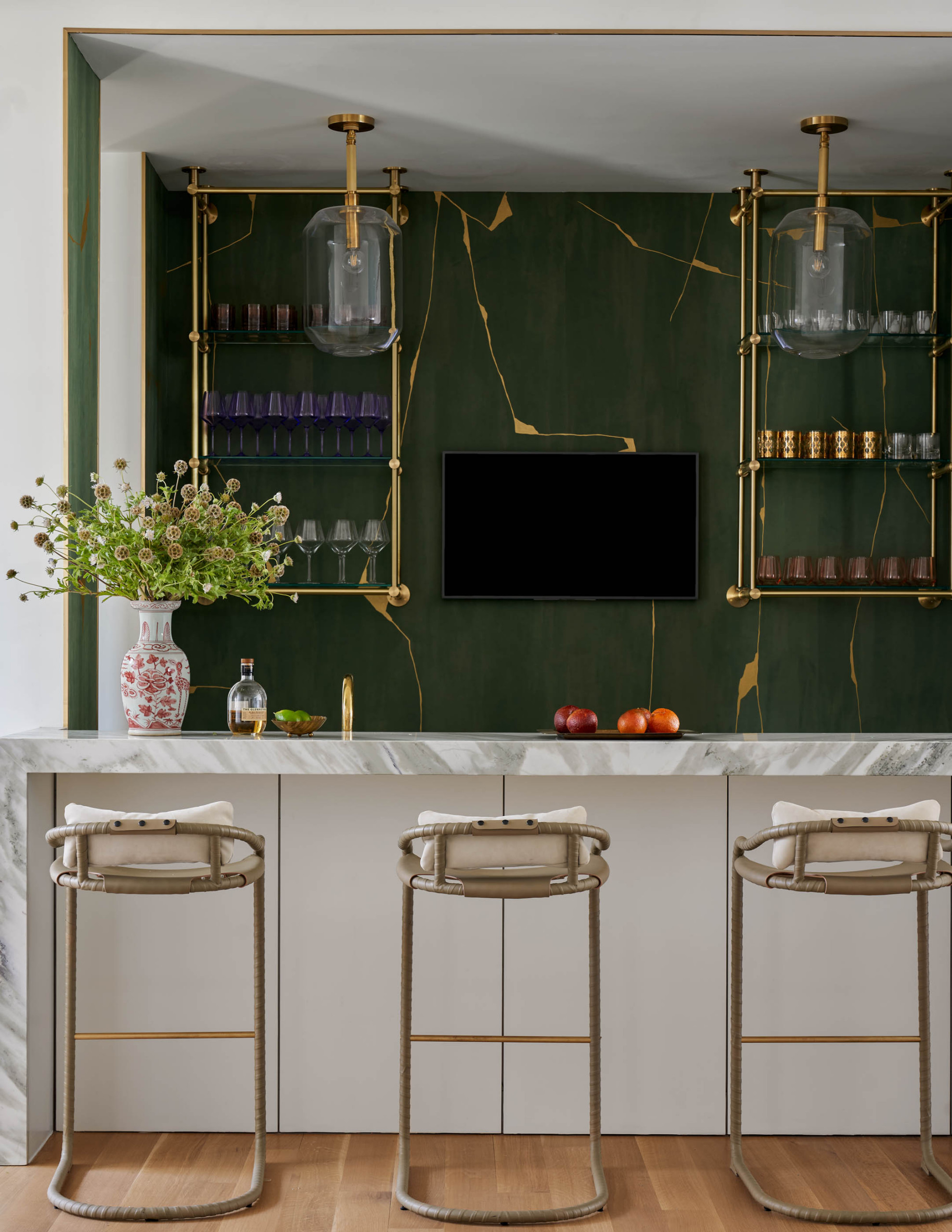 Elegant home bar with marble countertop, green and gold accent wall, and modern bar stools.