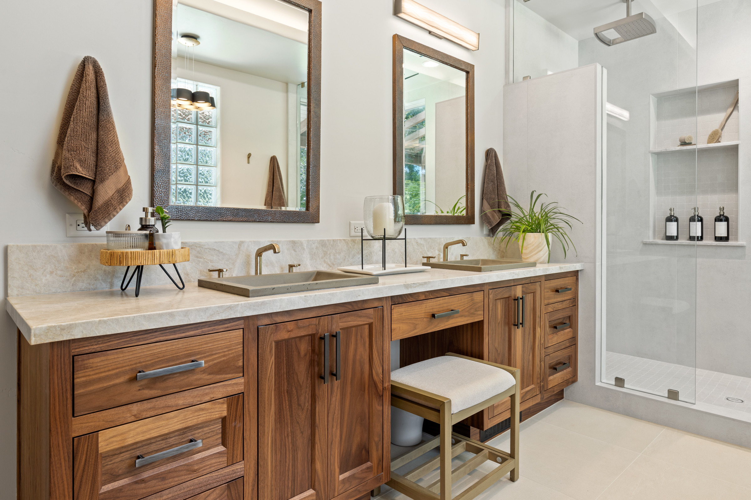 Bathroom with wooden double vanity, modern mirrors, and glass shower