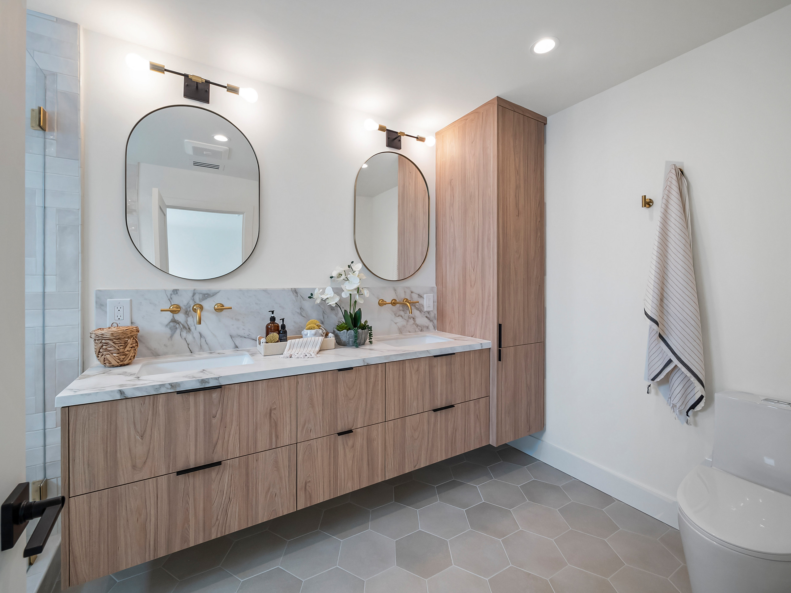 Modern bathroom with floating wood vanity, marble backsplash, and round mirrors