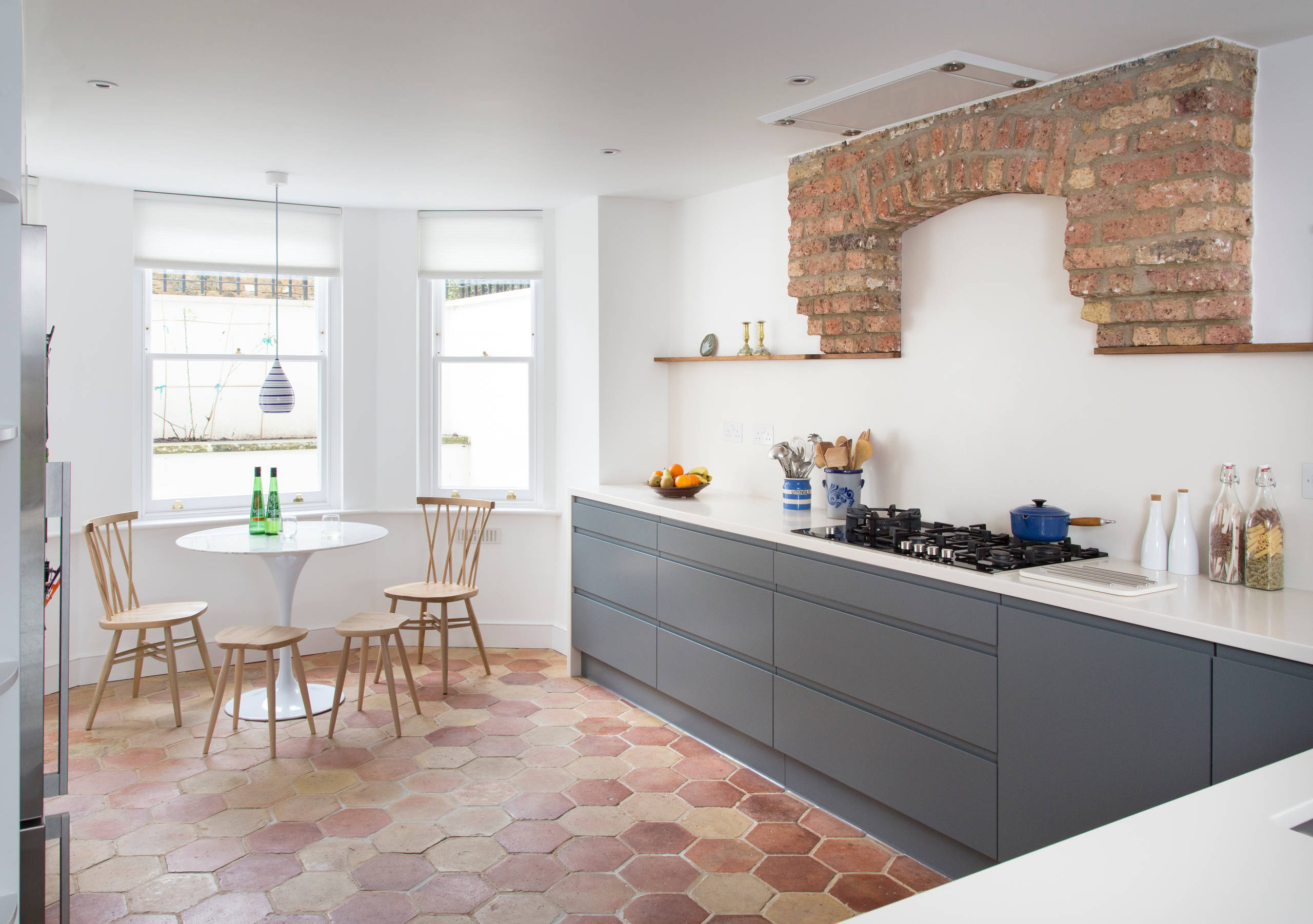 Modern kitchen with hexagon terracotta floor tiles, gray cabinets, and exposed brick arch