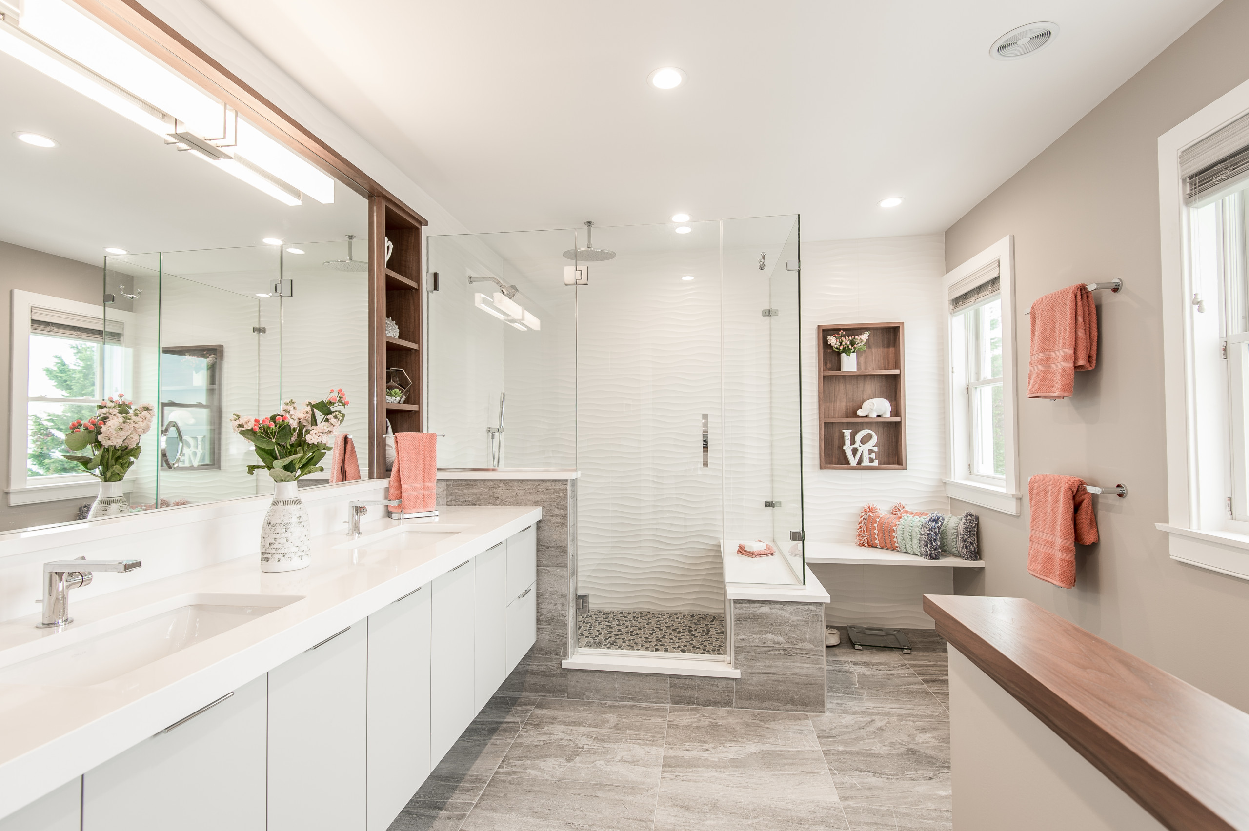 Bright modern bathroom with glass shower, long vanity, and coral accents