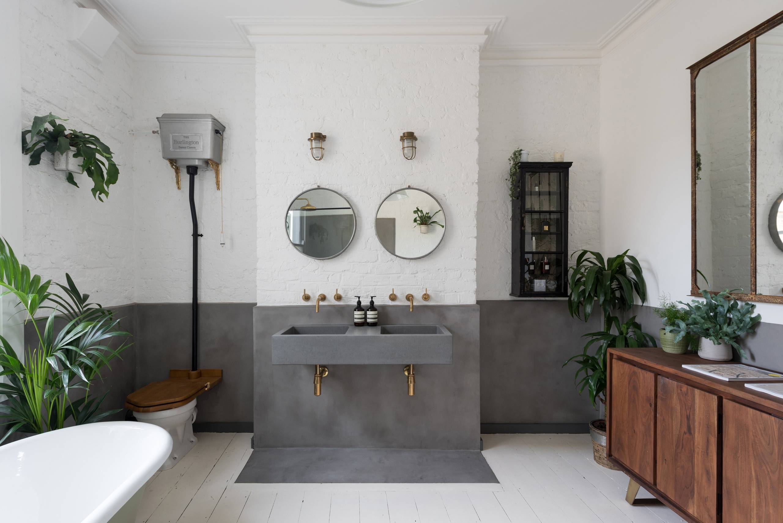 Industrial-style bathroom with concrete sink, round mirrors, and greenery
