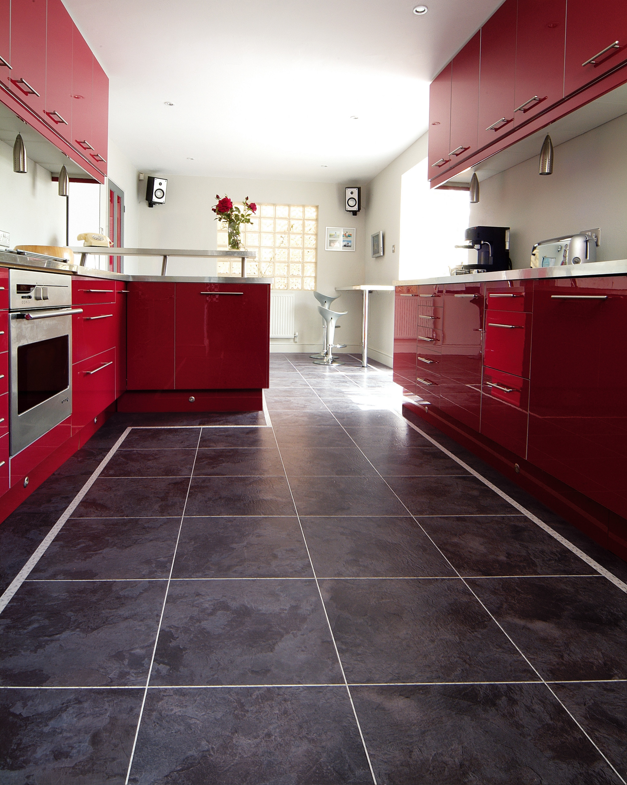 Modern kitchen with glossy red cabinets, stainless steel appliances, and dark tiled flooring