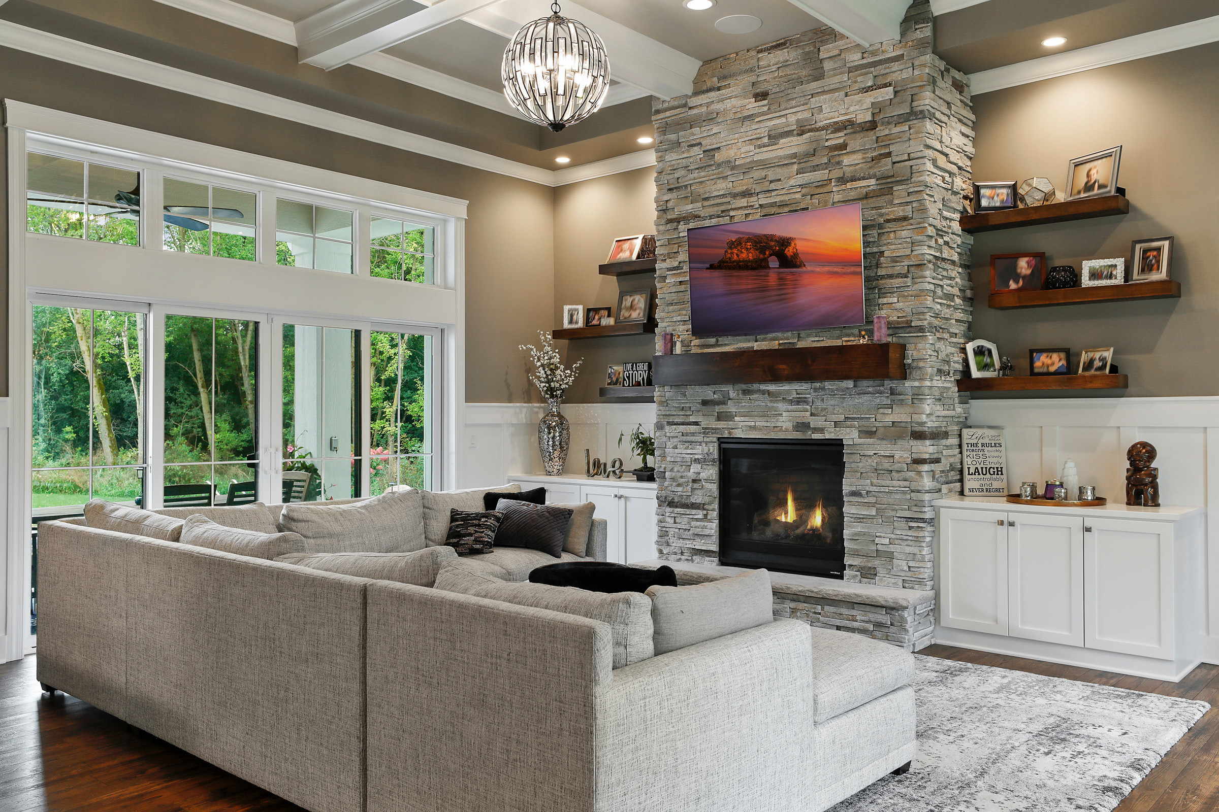 Modern living room with stone fireplace, sectional sofa, and large windows.