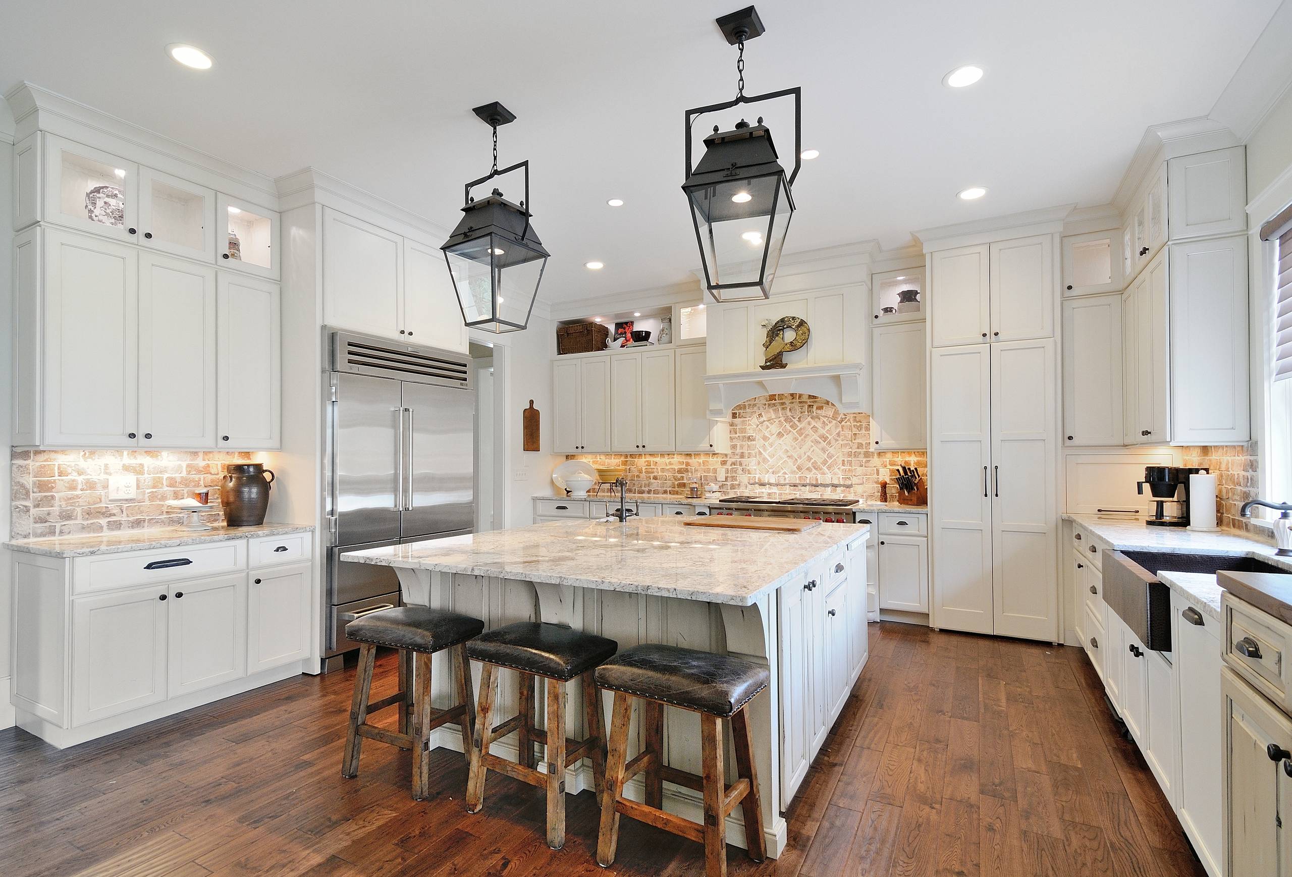Rustic farmhouse kitchen with white cabinets, brick backsplash, and large island.