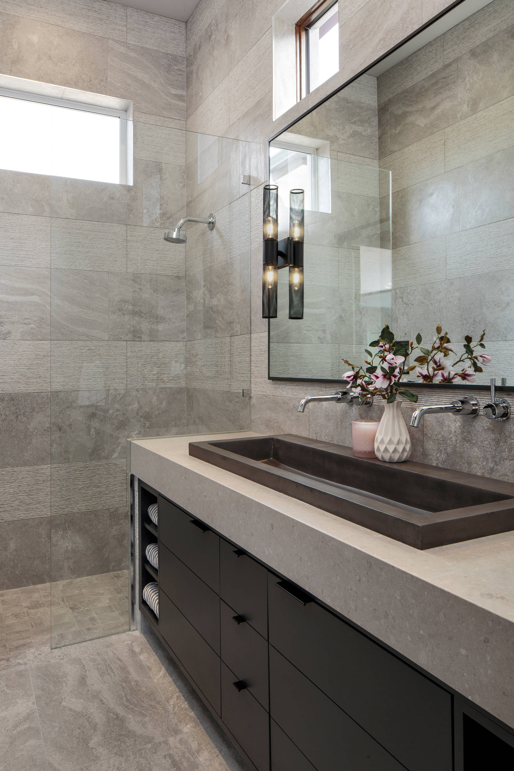 Modern bathroom with gray stone tiles, sleek black vanity, and elongated sink basin