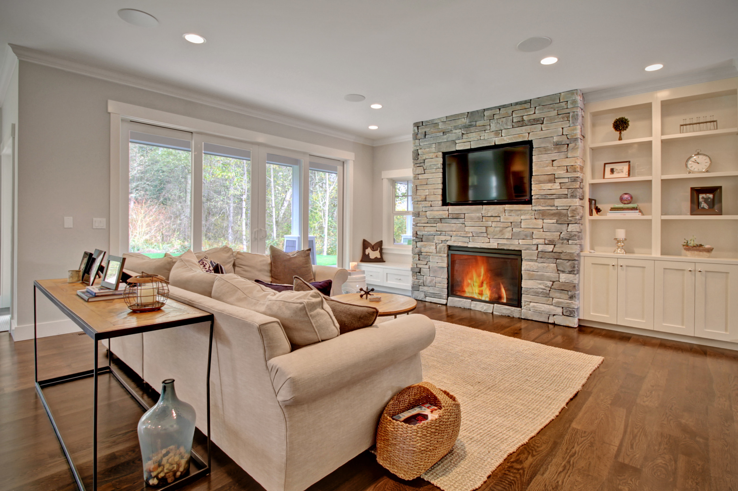 Modern living room with stone fireplace, built-in shelves, and large windows.