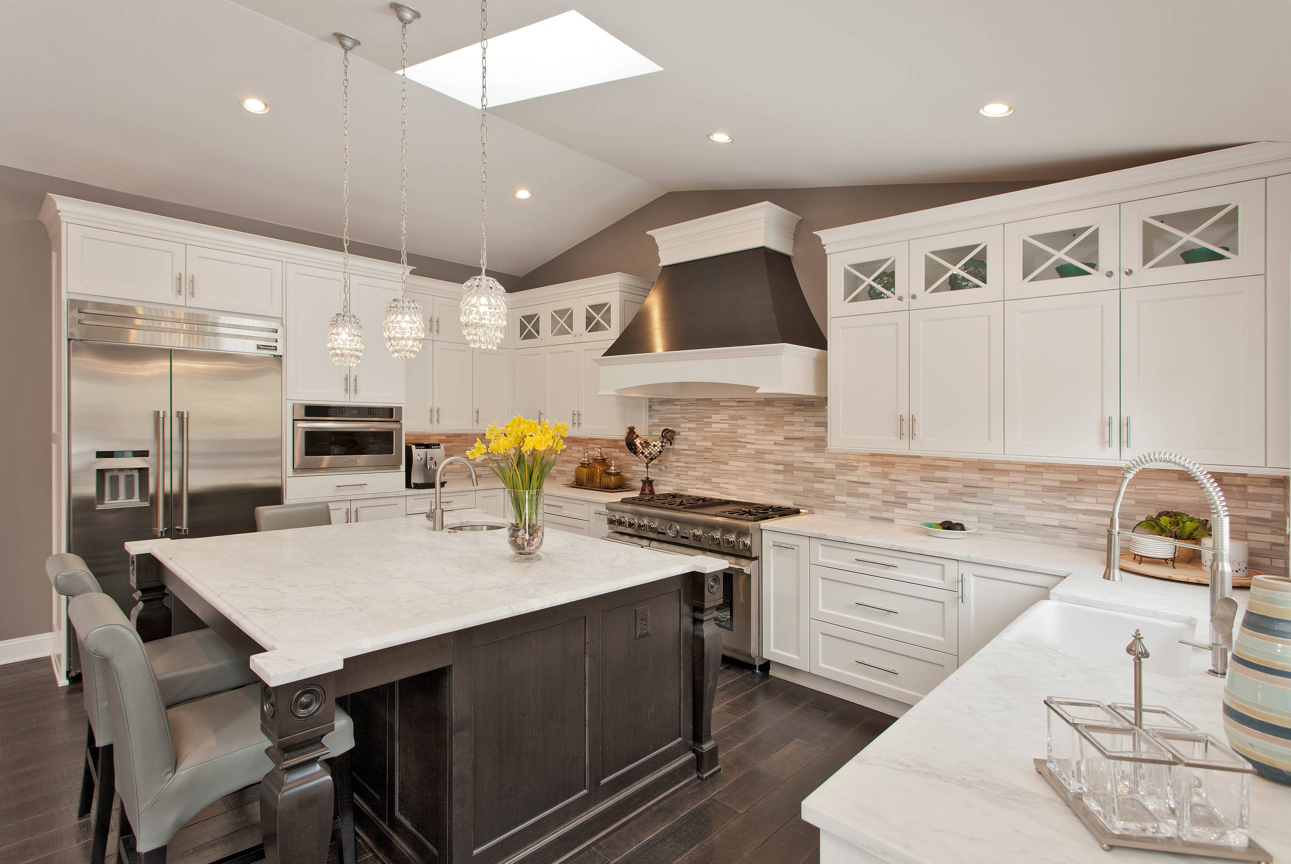 Luxury kitchen with white cabinets, large marble island, and stainless steel appliances.