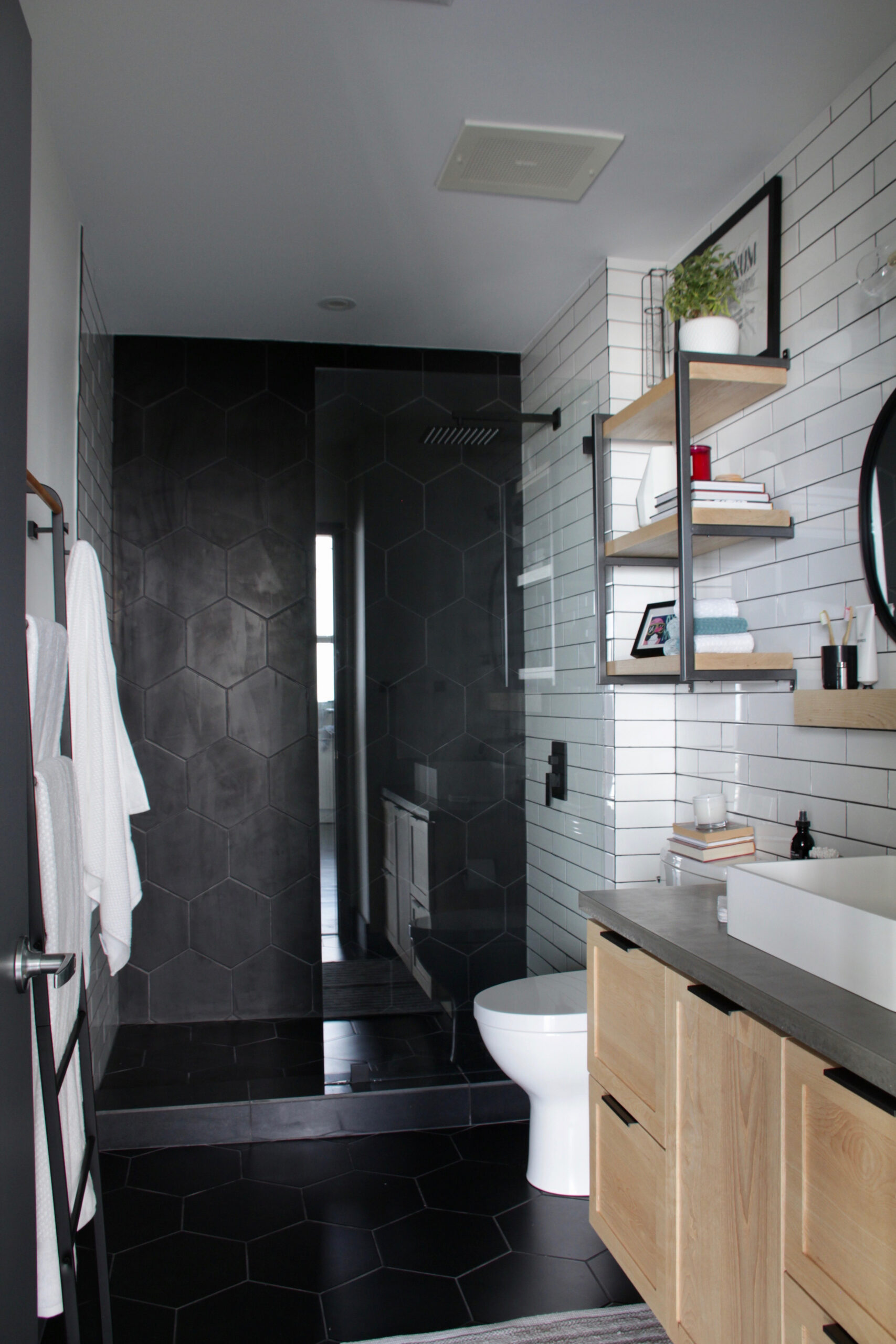 Modern bathroom with sleek black and white design, featuring hexagonal tiles, open shelving, and a minimalist aesthetic.