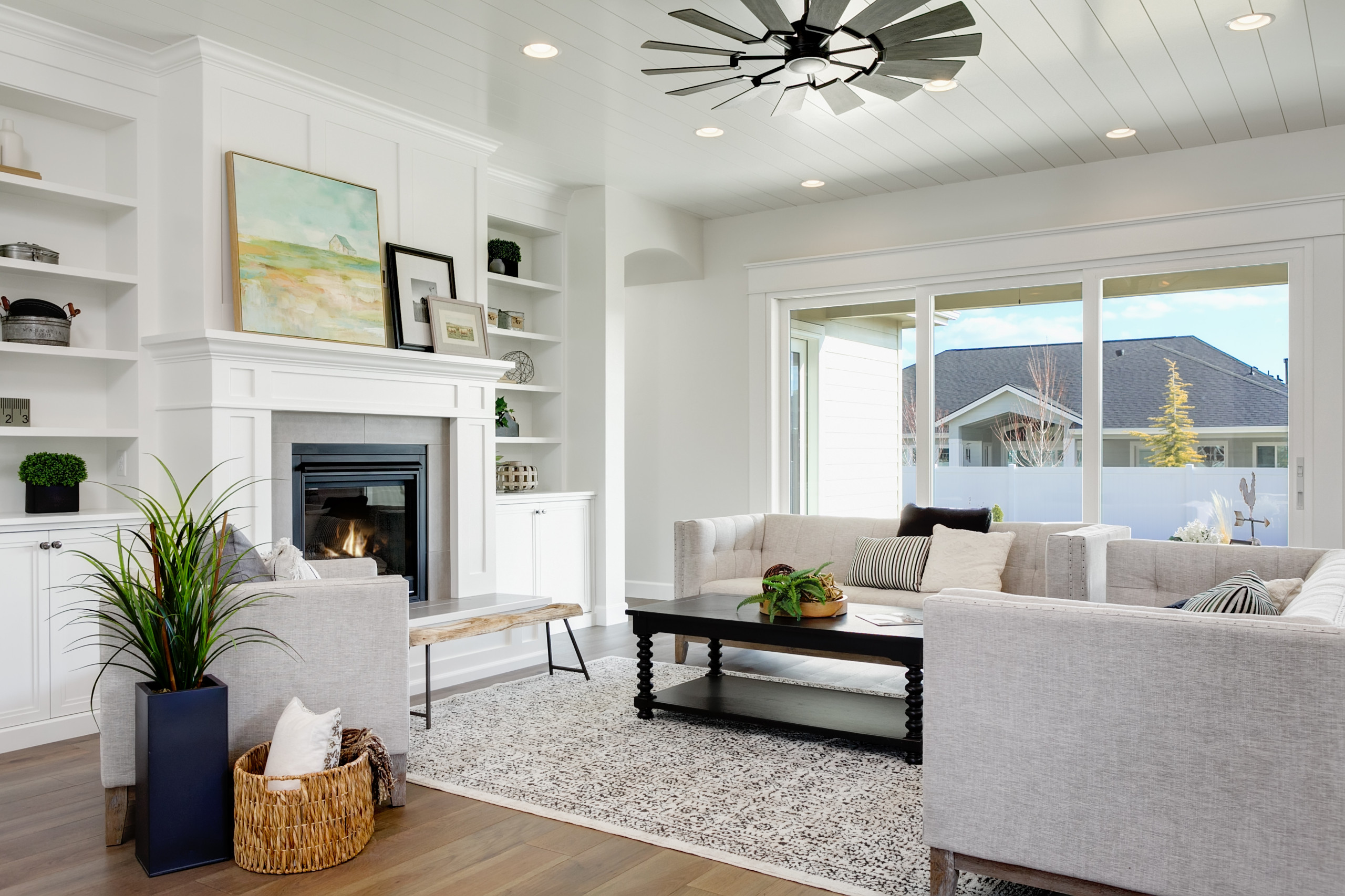 Bright living room with white fireplace, built-in shelving, and large windows