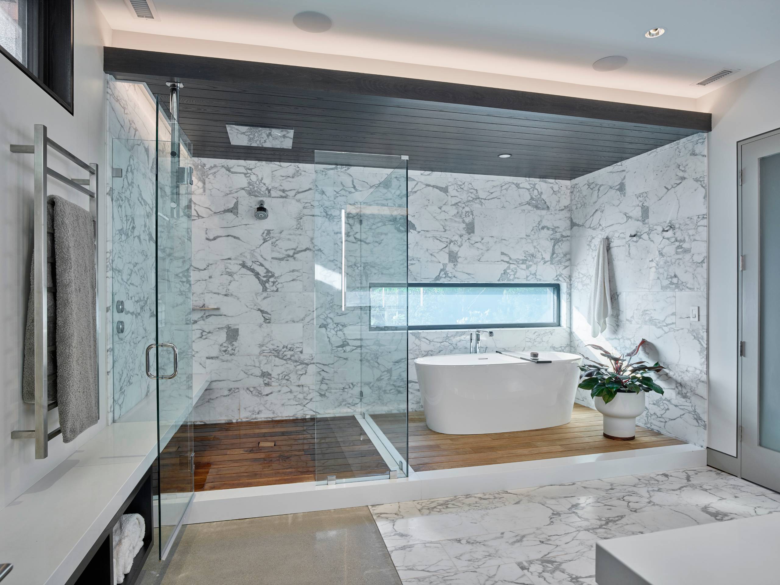 Luxury bathroom with marble walls, glass shower, and freestanding tub